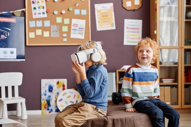 Kleiner Junge mit vr-Headset, der sich Videos ansieht und virtuelle Spiele spielt, während er neben einer glücklichen Klassenmutter sitzt