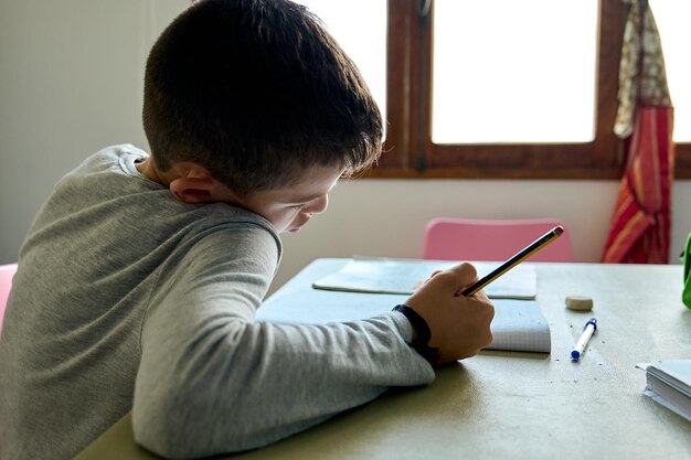 Kleiner Junge saß an einem Tisch und machte seine Hausaufgaben, allein, zu Hause