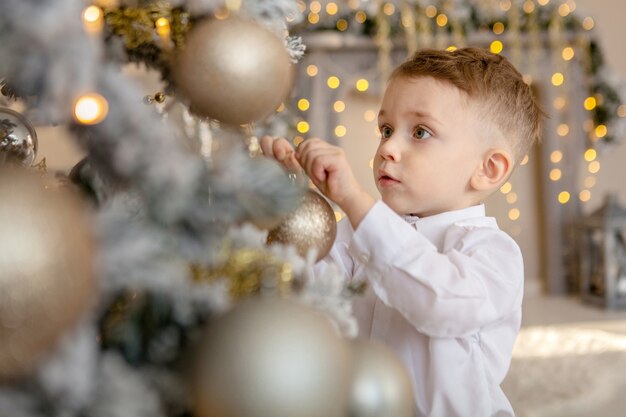 Kleiner Junge schmückt einen Weihnachtsbaum für Weihnachten.