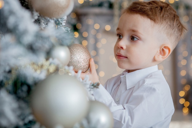 Kleiner Junge schmückt einen Weihnachtsbaum zu Weihnachten