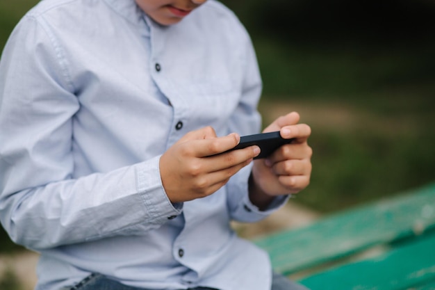 Kleiner Junge sitzt auf der Bank und spielt während der Schulferien Online-Spiele