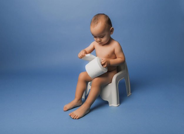 Kleiner Junge sitzt auf einem Töpfchen mit Toilettenpapier auf blauem Studiohintergrund.