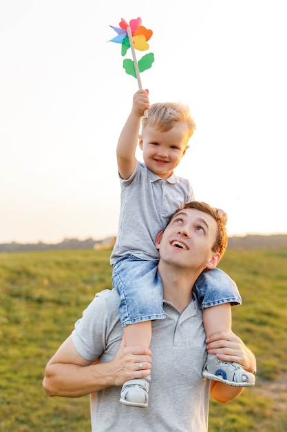 Foto kleiner junge sitzt auf papas schultern und spielt mit bunter windmühle vater und sohn haben spaß