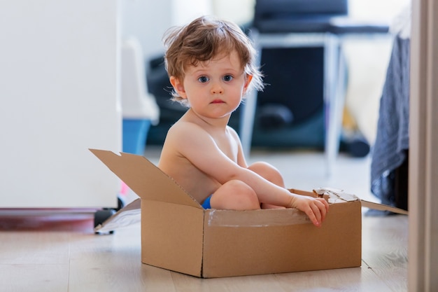 Kleiner Junge sitzt zu Hause in einer Kiste auf dem Boden