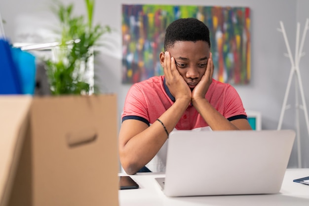 Kleiner Junge sitzt zusammengesunken vor Computer-Requisiten, Hände unter Gesicht, schlechte Nachrichten, Geldverlust, Überarbeitung