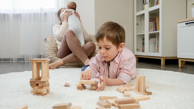 Kleiner Junge spielt auf dem Teppich neben seiner Mutter und seinem kleinen Bruder und schenkt den Kindern Glück