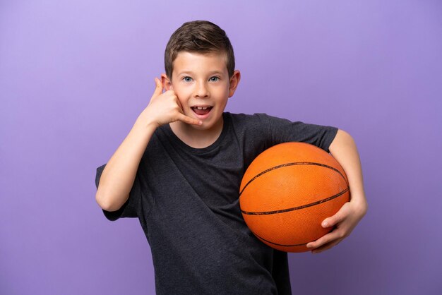 Kleiner Junge spielt Basketball isoliert auf violettem Hintergrund und macht eine Telefongeste. Ruf mich zurück