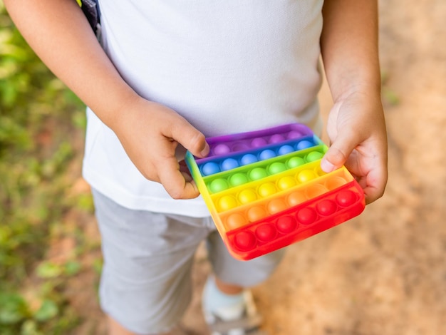 Kleiner Junge spielt mit einem quadratischen Gummi-Fidget-Spielzeug, dem Regenbogenfarbenen Anti-Stress-Taktilspielzeug