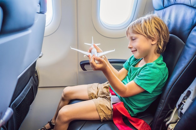 Kleiner Junge spielt mit Spielzeugflugzeug im kommerziellen Düsenflugzeug, das im Urlaub fliegt