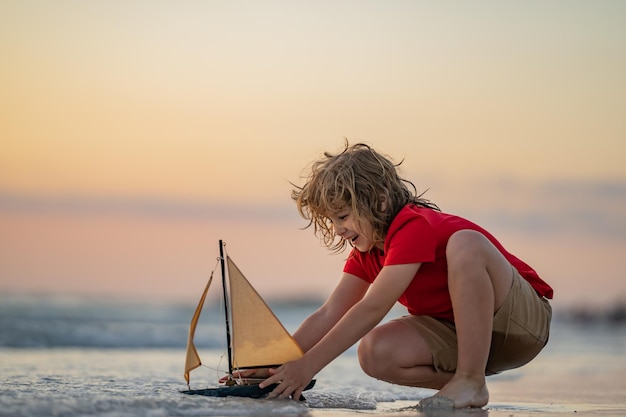 Kleiner Junge spielt während der Sommerferien, Kindheit und Jugend mit Spielzeugboot in den Meereswellen am Strand