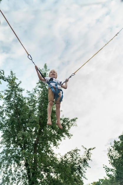 Kleiner Junge springt in einem Vergnügungspark auf den Seilen hoch in den Himmel Schuljunge hat Spaß im Themenpark Sommerurlaub