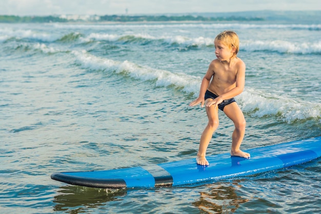 Kleiner Junge Surfen am tropischen Strand Kind auf Surfbrett auf Ozeanwelle Aktive Wassersportarten für Kinder Kid Schwimmen mit Brandung Surfunterricht für Kinder