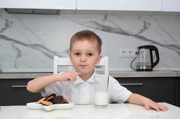 Kleiner Junge trinkt Milch und isst morgens Kekse in der Küche.