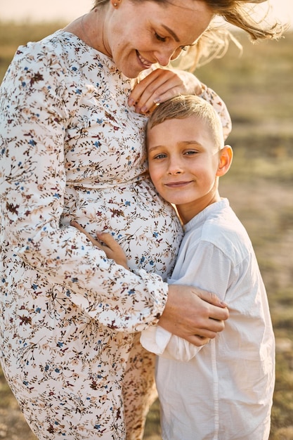 Kleiner Junge umarmt den Bauch seiner schwangeren Mutter im Freien