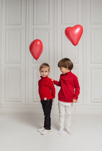 Kleiner Junge und Mädchen, die Herzballons auf weißem Hintergrund halten