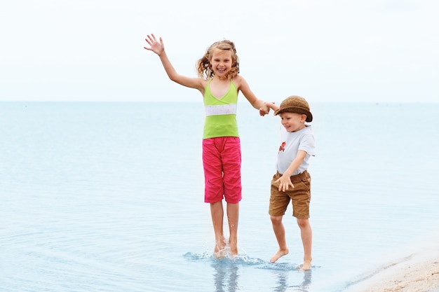 Kleiner Junge und Mädchen springen und haben Spaß im Wasser am Strand am Meer