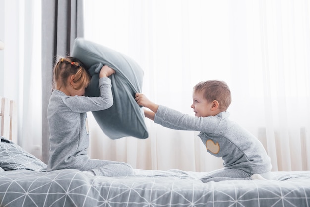 Kleiner Junge und Mädchen veranstalteten eine Kissenschlacht auf dem Bett im Schlafzimmer. Freche Kinder schlagen sich gegenseitig Kissen. Sie mögen diese Art von Spiel.