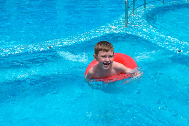 Kleiner Junge von 7 Jahren, der im Pool mit aufblasbarem Gummiring schwimmt Lustiges, glückliches Kind, das im Aquapark spielt Sommerferien und Urlaubsreise- und Tourismuskonzept