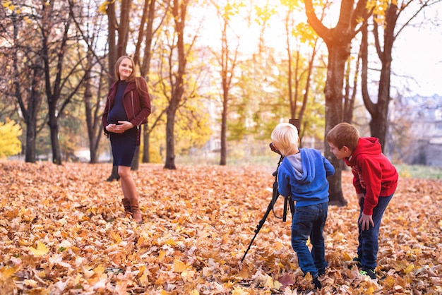 Kleiner Junge zwei mit einer großen Spiegelreflexkamera auf einem Stativ. Machen Sie ein Foto von ihrer schwangeren Mutter. Familienfotosession