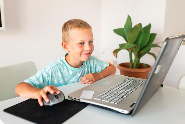 Kleiner junger Schuljunge, der in einer virtuellen Klasse studiert und eine Videokonferenz auf dem Laptop mit Lehrer f hat