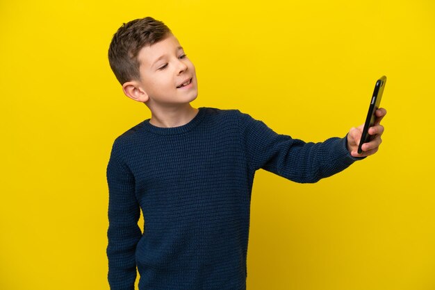 Kleiner kaukasischer Junge isoliert auf gelbem Hintergrund, der ein Selfie macht