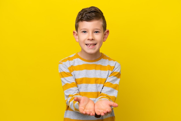 Kleiner kaukasischer Junge isoliert auf gelbem Hintergrund, der einen imaginären Copyspace auf der Handfläche hält, um eine Anzeige einzufügen