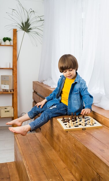 Kleiner kaukasischer Junge mit braunen Haaren sitzt auf den Stufen und spielt Schach. Entwicklung des Kindes