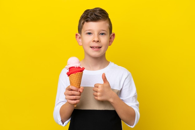 Kleiner kaukasischer Junge mit einem Cornet-Eis isoliert auf gelbem Hintergrund mit einer Daumen-hoch-Geste