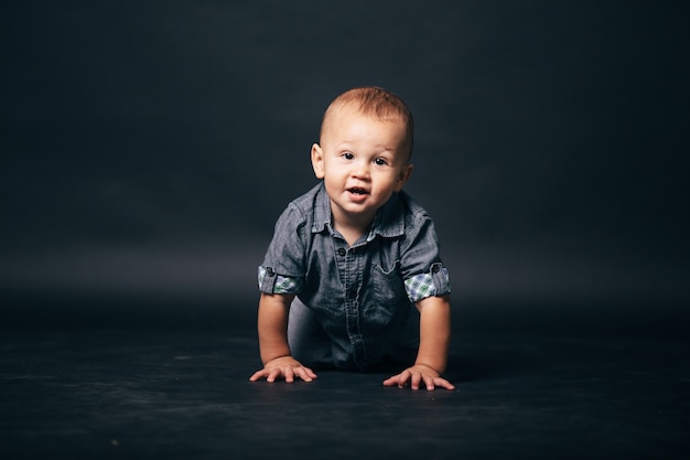 Kleiner Kinderjunge von einem Jahr im Denim-Outfit auf einem grauen Studiohintergrund. süßes Baby lächelt.