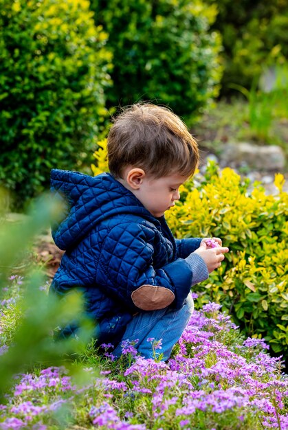 Kleiner Kleinkind, der mit Blumen im Garten spielt