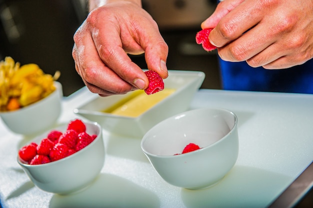 Kleiner Kuchen auf einem Teller. Hand legt Minze auf Dessert. Chefkoch bereitete einen Käsekuchen zu. Kochen als Kunst.