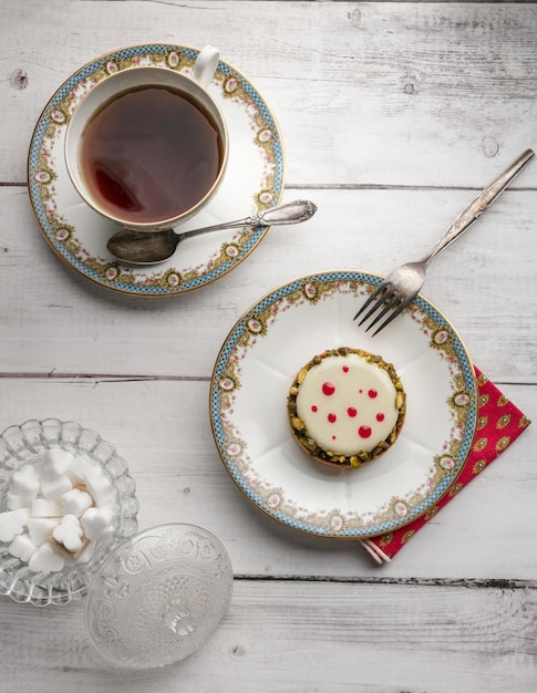 Kleiner Kuchen in einem alten Teller mit einer Tasse Tee auf einem Holztisch