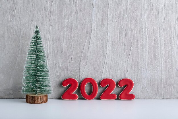 Kleiner künstlicher Weihnachtsbaum und rote Zahlen 2022 vor einer grauen Wand. Konzept des neuen Jahres. Platz kopieren.