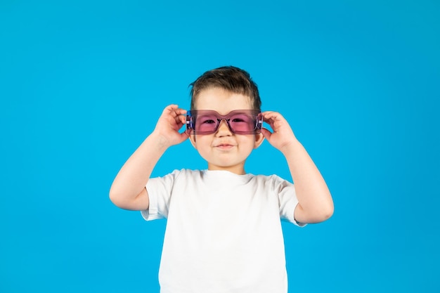 Kleiner lächelnder Junge in weißem T-Shirt mit violetter Brille auf blauem Hintergrund Foto in hoher Qualität