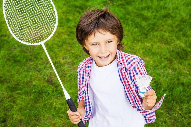 Kleiner Meister. Draufsicht eines glücklichen kleinen Jungen, der Badmintonschläger und Federball hält, während er auf grünem Gras steht