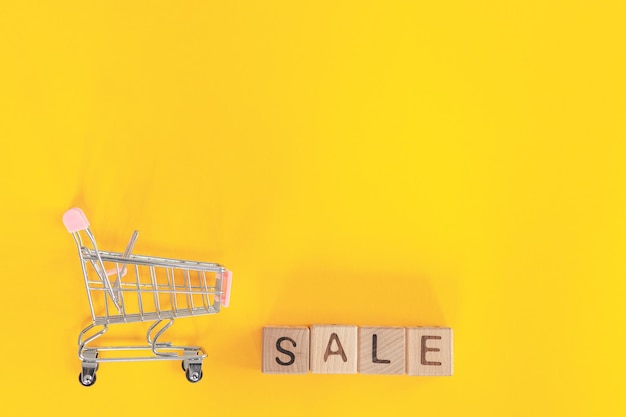 Kleiner Metallwagen und Wortverkauf auf gelbem Hintergrund Einkaufskonzept
