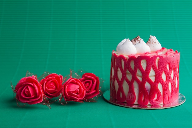 Kleiner roter Zuckerguss-Cupcake mit cremigem Topping und roten Rosen auf grünem Hintergrund