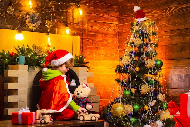 Kleiner santa-junge, der mit spielzeug im schönen neujahrs-dekorierten raum spielt schönes baby genießt weihnachten
