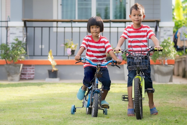 Kleiner süßer asiatischer Junge und Mädchen auf Fahrrädern, Blick in die Kamera, Schwester und Bruder auf dem Spielplatz zu Hause