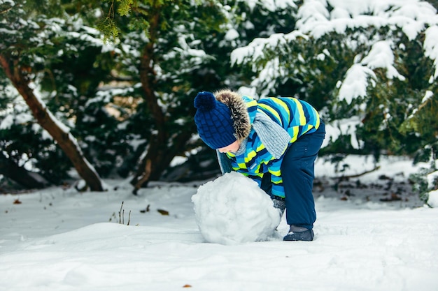 Kleiner süßer Junge, der einen Schneemann macht, der einen großen Schneeball rollt