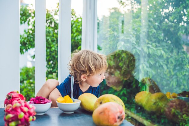 Kleiner süßer Junge, der Mango auf der Terrasse isst.