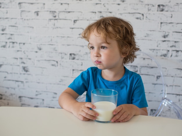 Kleiner süßer Junge im T-Shirt, das Milch trinkt