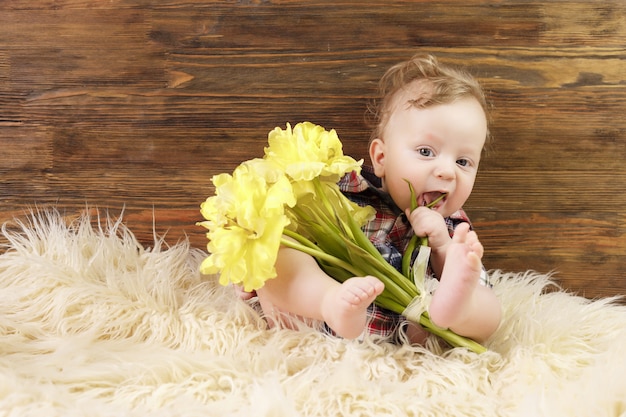 Kleiner süßer Junge sitzt mit gelben Tulpen in seiner Hand