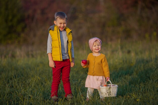 Kleiner süßer Junge und Mädchen spielen im Herbstgarten. Bruder und Schwester mit roten Äpfeln. Warmer und heller Herbst.