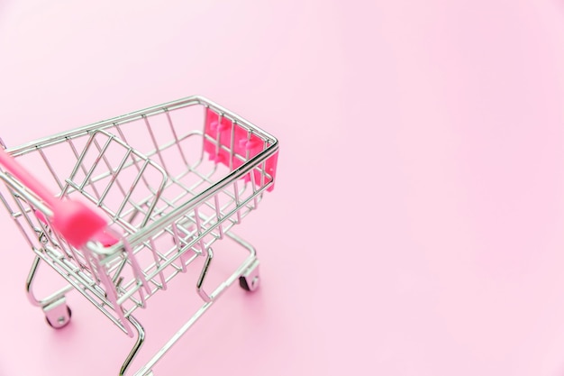Kleiner Supermarkt-Lebensmittel-Schiebewagen für Einkaufsspielzeug mit Rädern, isoliert auf rosa pastellfarbenem...