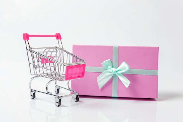Kleiner Supermarkt-Lebensmittel-Schubkarren zum Einkaufen von Spielzeug mit rosafarbener Geschenkbox isoliert auf weißem Hintergrund Sale buy mall market shop Consumer concept Kopieren Sie Platz