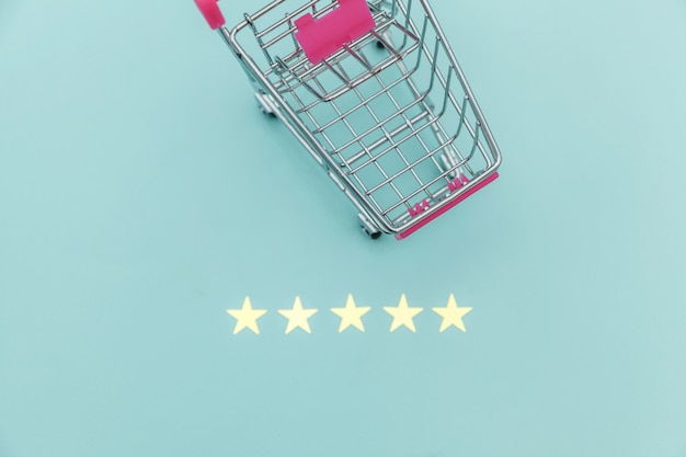 Kleiner Supermarktlebensmittelgeschäft-Stoßwarenkorb für Einkaufsspielzeug mit Rädern und der Bewertung mit 5 Sternen lokalisiert auf blauem Pastellhintergrund. Einzelhandelsverbraucher kaufen Online-Bewertung und Review-Konzept.