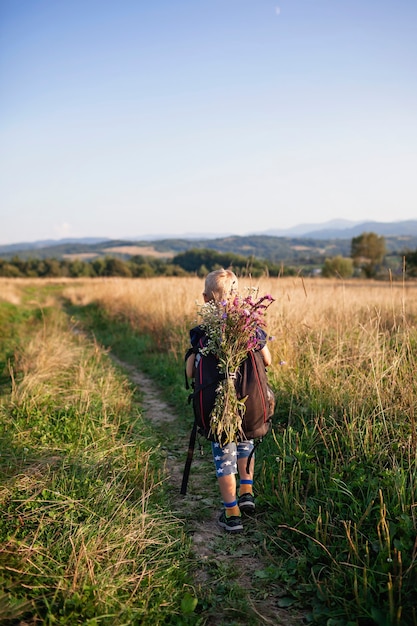 Kleiner Wanderer mit Rucksack kommt vom Berg und trägt einen Strauß Wildblumen Schönheit der Natur