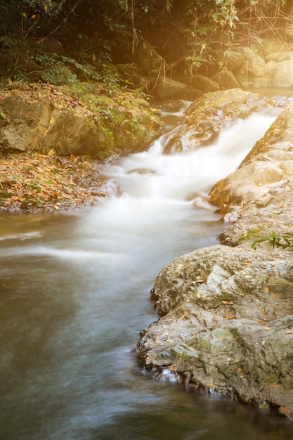 Kleiner Wasserfall mit Wasser, das bei strahlendem Sonnenschein über die Felsen im Wald spritzt und stürzt