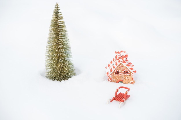 Foto kleiner weihnachtsbaum, schlitten und lebkuchenhaus im schnee im freien. frohe weihnachten. frohes neues jahr. foto in hoher qualität